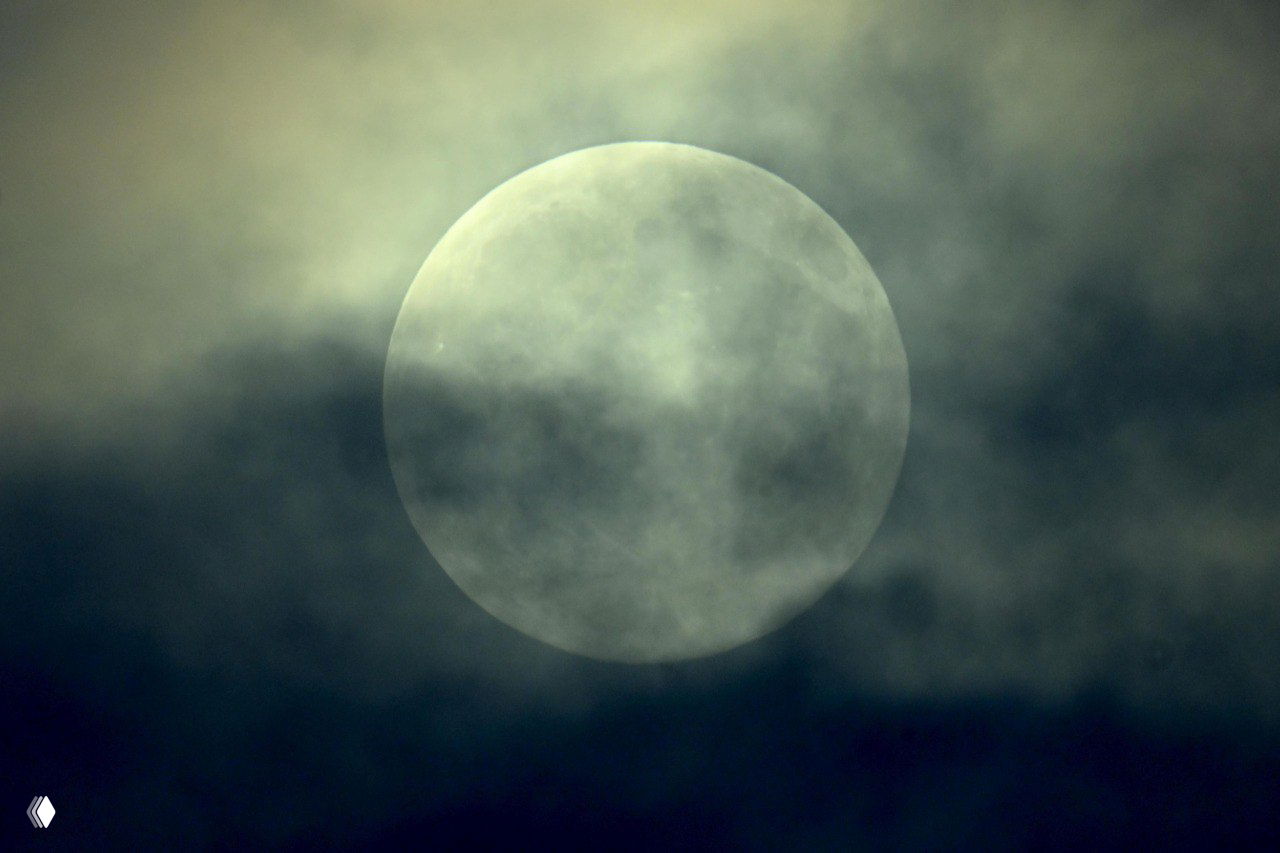 Крупный план полной Луны сквозь тонкие облака, атмосферная ночная фотография, демонстрирующая бледный диск Луны на тёмном небе во время суперлуния