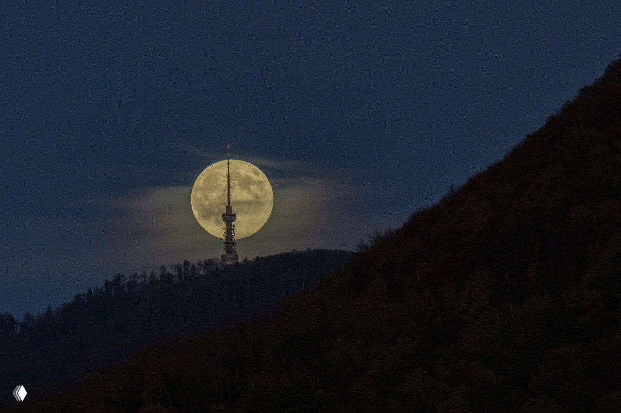 Полная Луна, поднимающаяся над старинным монастырским комплексом на закате, тёплые тона неба и контраст архитектуры с ярким лунным диском