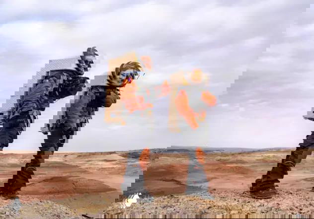 Два человека в оранжевых скафандроподобных костюмах с рюкзаками‑блоками на фоне марсианоподобного ландшафта Гоби — участники симуляции в экипировке.