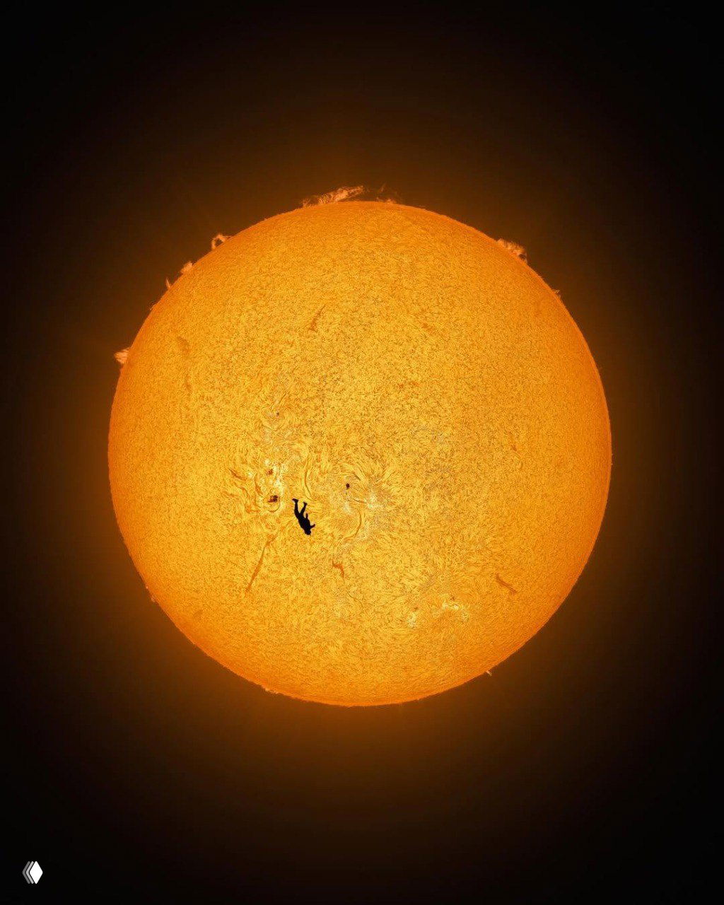 Полный диск Солнца на тёмном фоне: видна яркая солнечная поверхность и протуберанцы, вблизи центра — миниатюрный тёмный силуэт прыгающего человека.