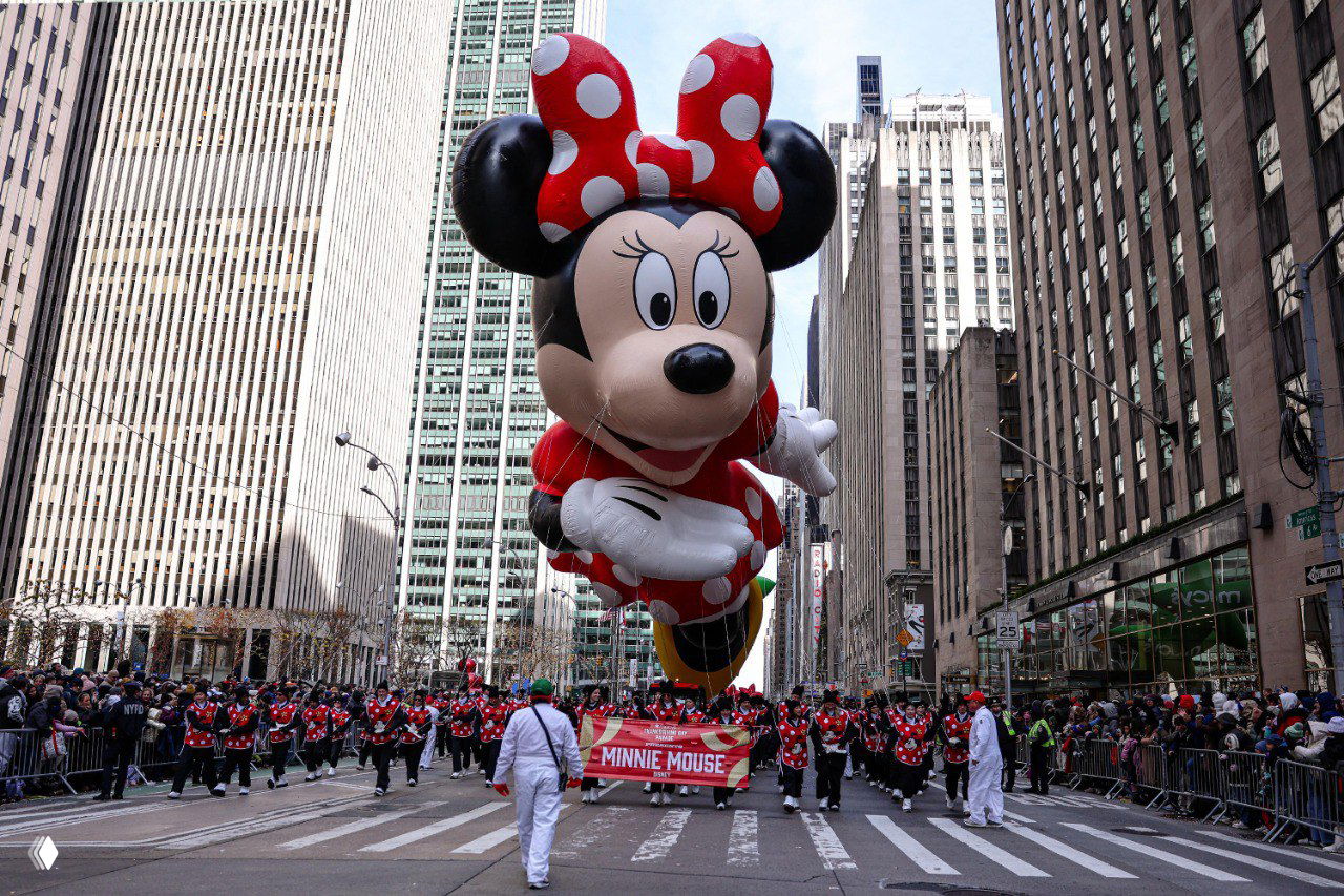 Минни Маус как крупный надувной шар сопровождается командой держателей и движется по улицам Манхэттена среди зрителей.