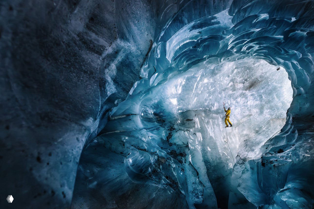 Альпинист в жёлтом костюме карабкается по ледяному куполу внутри ледника — атмосферный кадр из серий спортивных и приключенческих снимков.