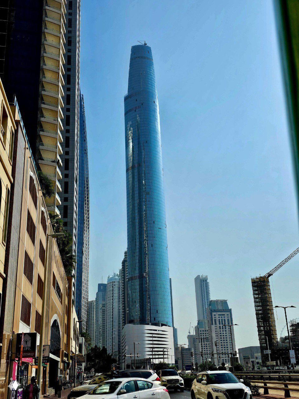 Небоскрёб Ciel Dubai Marina высотой 377 метров в деловом районе Дубая, стеклянный фасад на фоне голубого неба и автомобили на улице внизу