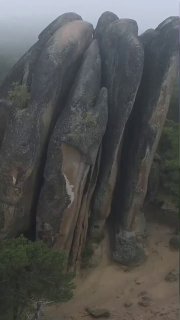 Вертикальные массивные гранитные столбы в тумане в национальном парке «Красноярские Столбы», видны трещины, лишайники и лес у подножия