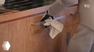 Робот NEO выполняет уборочную задачу на кухне: манипулятор держит тряпку и протирает поверхность, демонстрируется возможность работы с дверцами и шкафами.