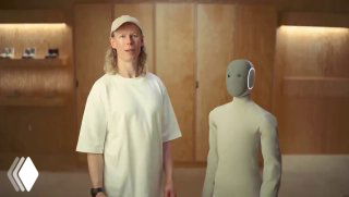 Человек демонстрирует рост и пропорции NEO на презентации: робот в вязаном 'костюме' стоит рядом с представителем компании, видно соотношение размеров.