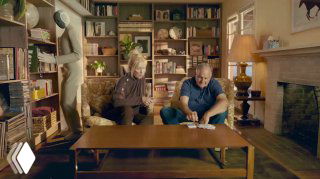 Сцена с пожилой парой и роботом NEO в домашней библиотеке: робот в мягкой одежде стоит возле полок, уютная обстановка и семейная сцена.