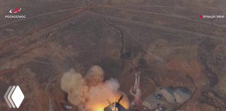 Аэрофотоснимок старта на Байконуре: вид сверху на пусковую площадку, столб дыма и пламени вокруг ракеты в момент подъёма.