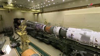 Ракета‑носитель и транспортировочная платформа внутри ангара космодрома Байконур перед вывозом на стартовую площадку; кадр распространён госкорпорацией Роскосмос.