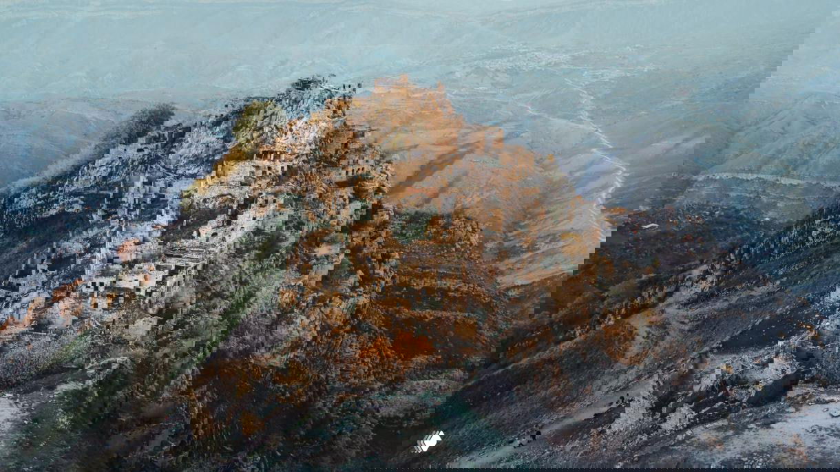 Панорамный вид на Аул Гамсутль и окружающие ущелья: развалины домов, редкие деревья и извилистые тропинки в долине.