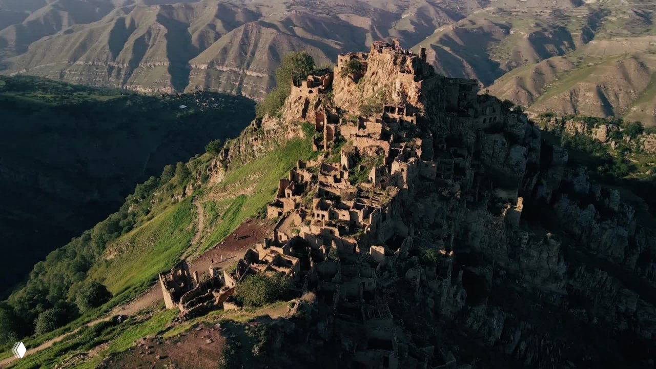 Аэровид на горный аул Гамсутль с зелёными склонами: разрушенные каменные дома на гребне среди долин и хребтов.