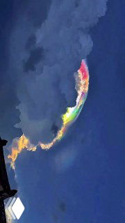 Яркая иризация на краю облака в тёмном небе: радужная полоска с красными и зелёными тонами на облачной структуре.