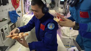 Китайский тайконавт в скафандре держит куриное крылышко в орбитальном модуле — иллюстрация эксперимента с грилем в космосе.