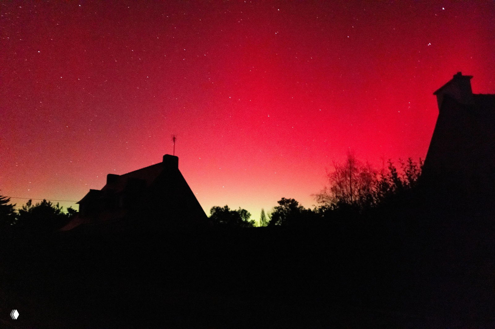 Зелёное и красное сияние над жилой улицей: волна света над крышами домов, тёмные силуэты зданий и ночные уличные фонари внизу кадра.