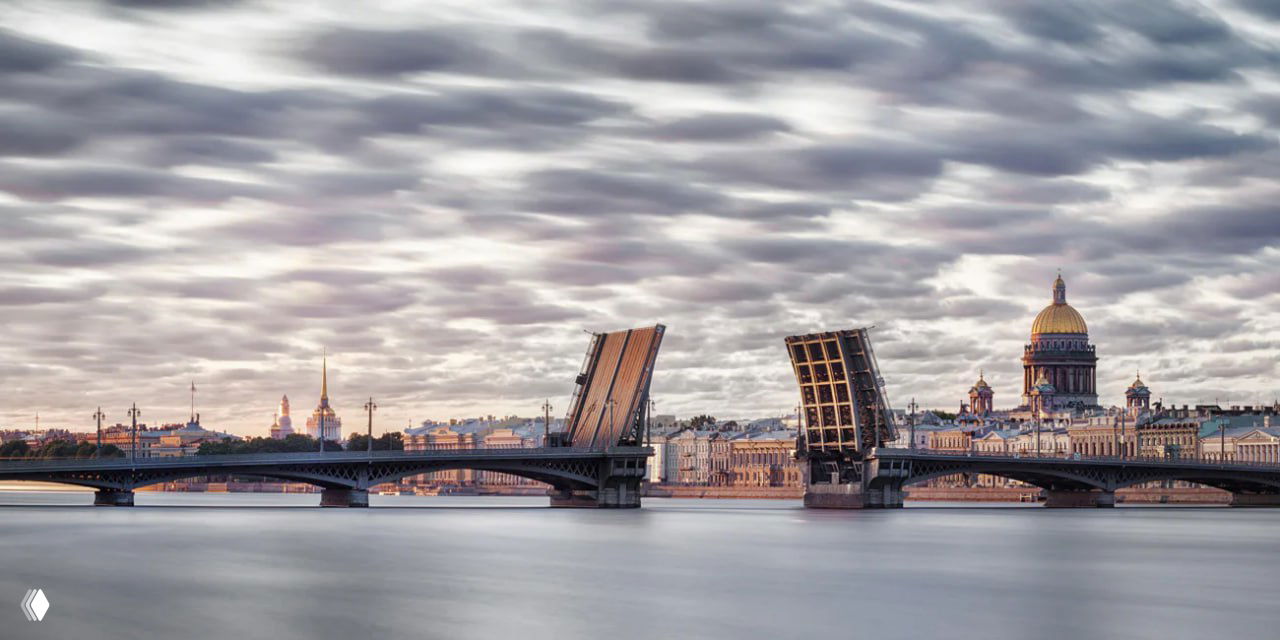 Современная фотография разведённого моста через Неву с развёрнутыми пролетами и панорамой Петербурга, заметен купол Исаакиевского собора.