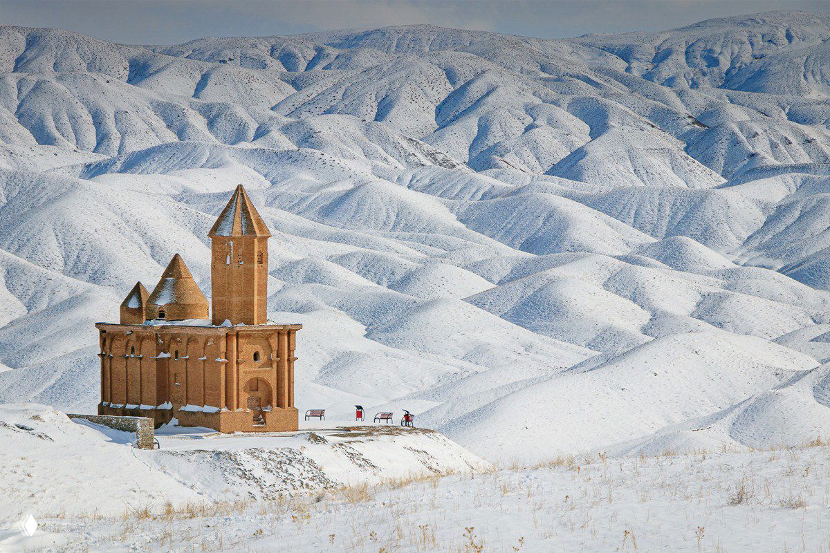 Армянская церковь Святого Иоанна на фоне заснеженных холмов в округе Шабестар, зимний пейзаж с небольшими фигурами людей у здания