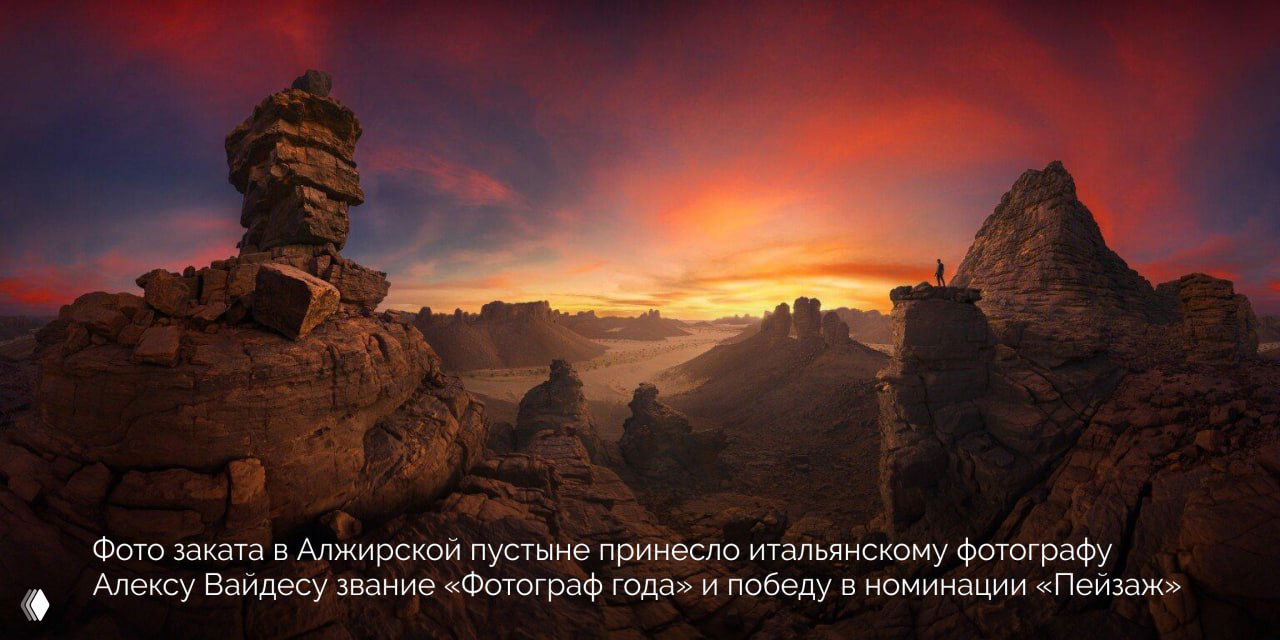 Панорамный снимок заката в алжирской пустыне с широким горизонтом, скалистыми выступами и крошечной фигурой человека на фоне огненного неба.