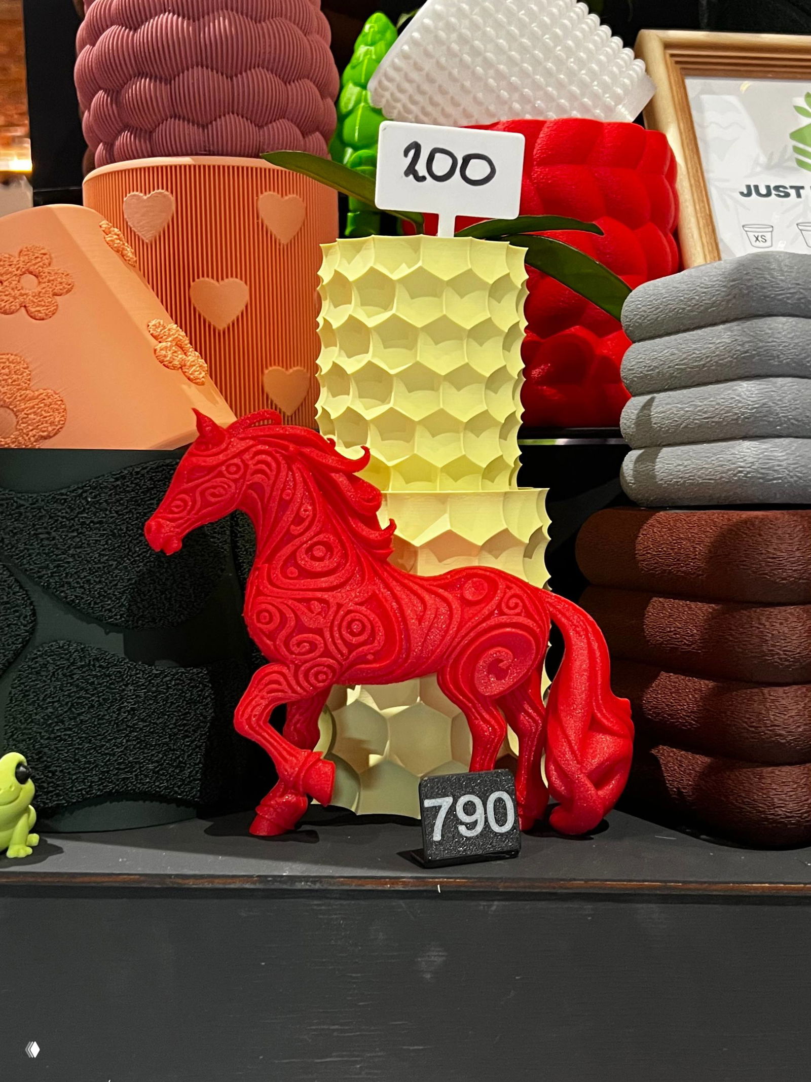 Крупный план декоративной витрины-прилавка: красная фигурка коня на фоне текстурированных горшков и ценником «790», яркая цветовая палитра.