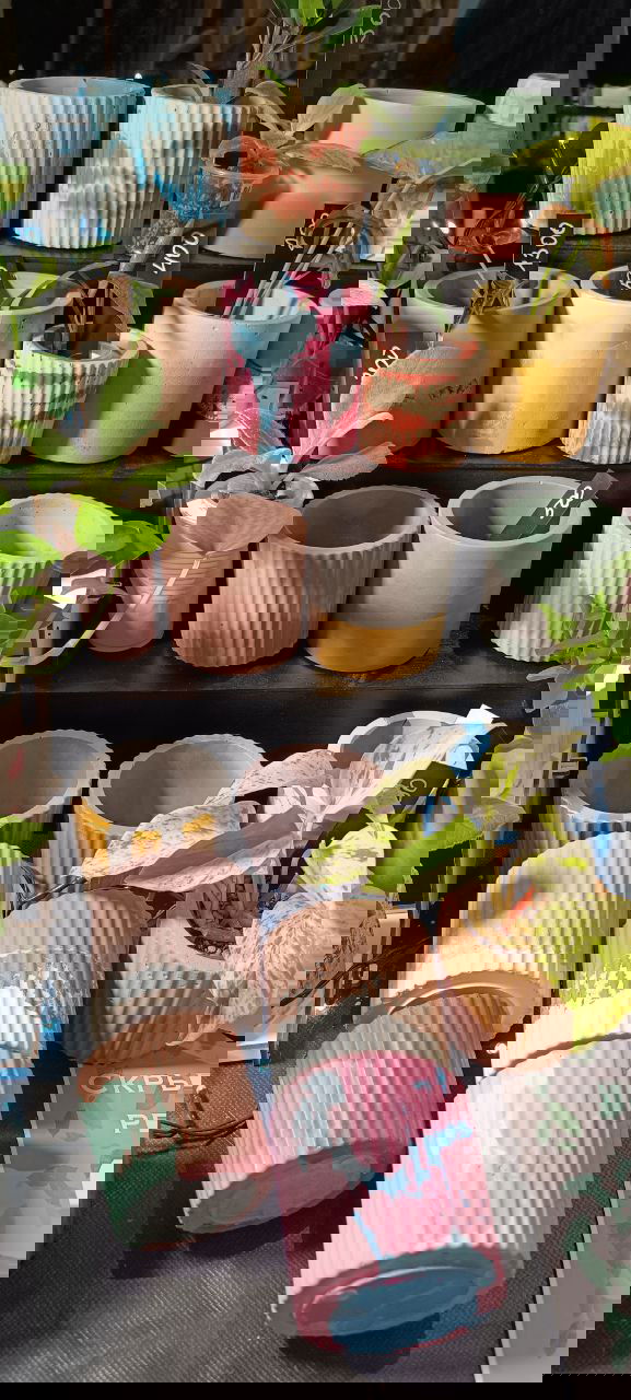 Ряд маленьких цветных горшков и кашпо из керамики и гипса на многоуровневой подставке; яркие мазки краски и разные фактуры на стенде маркета в Казани.