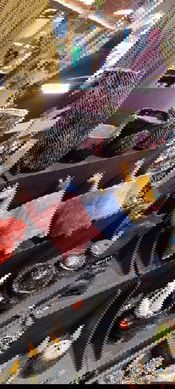 Стойка с оригинальными фигурными керамическими кашпо ручной работы: цветные животные и причудливые формы, подсвеченные лампой на ярмарке цветов в Казани.