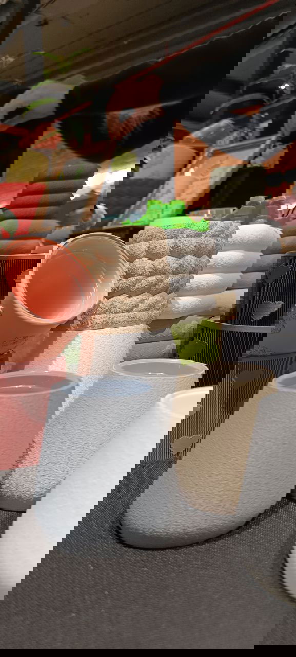 Матовые и рельефные кашпо пастельных тонов крупным планом, на заднем фоне — другие продавцы и детали ярмарки растений на мероприятии Green Market в Казани.