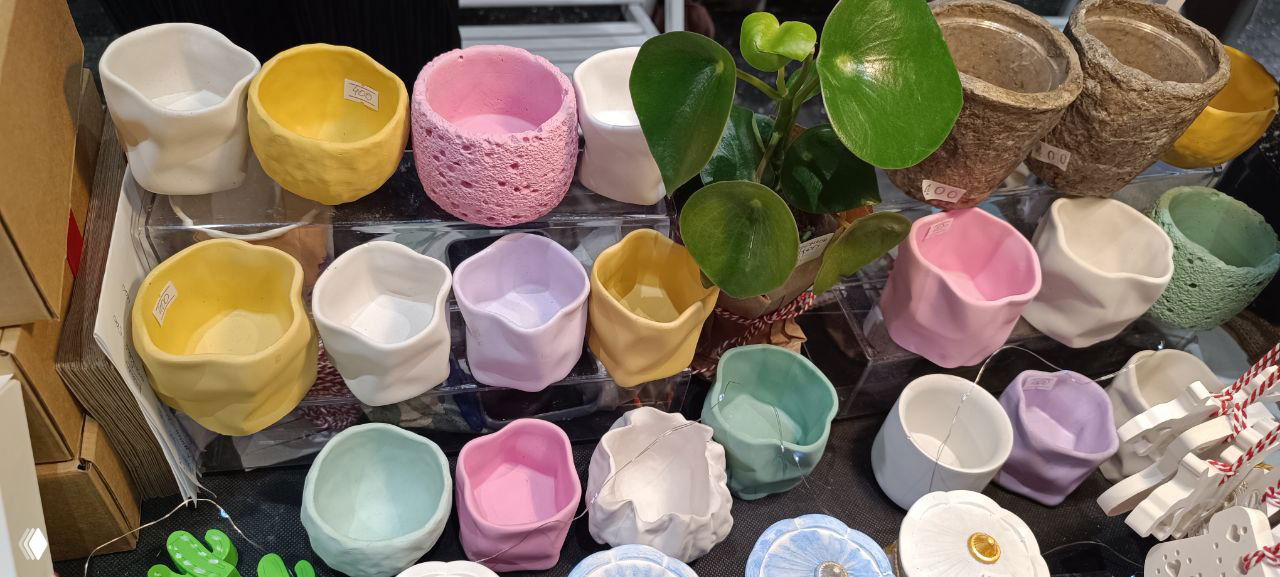 Мелкие декоративные горшочки и кашпо в форме цилиндров и кубов, разноцветные и текстурные, аккуратно разложены на витрине на цветочном маркете в Казани.