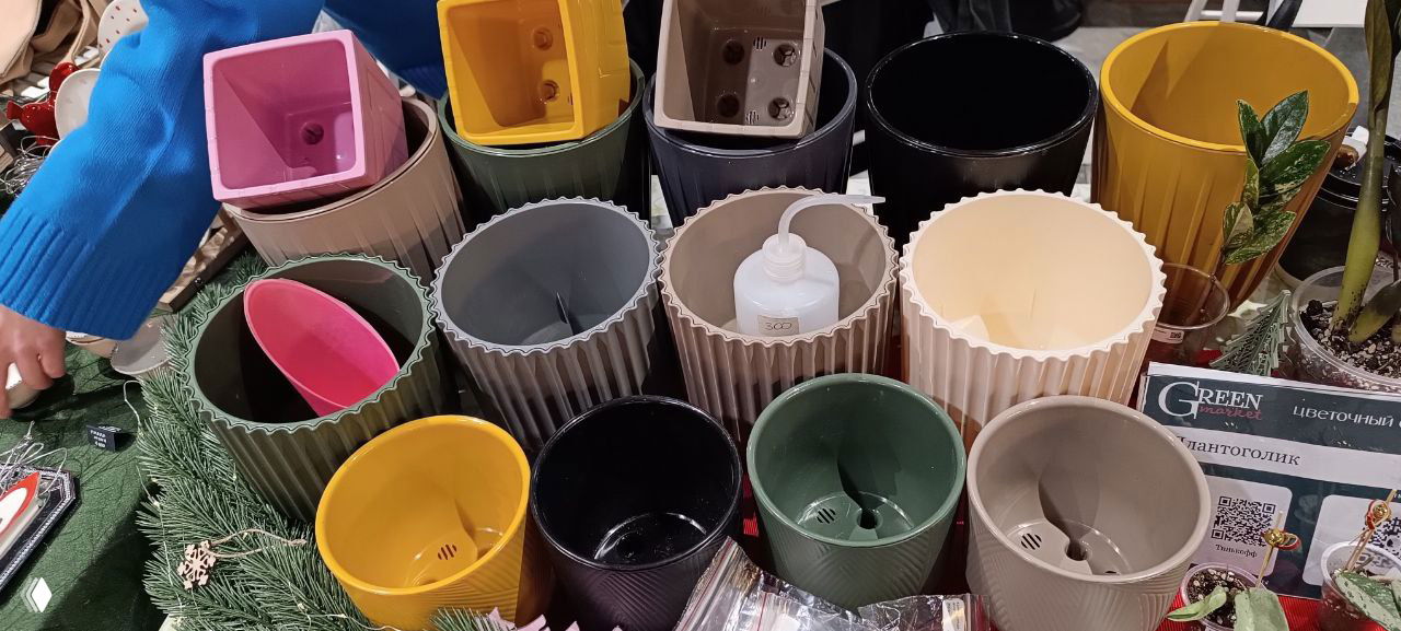 Ряд кашпо разной формы: цилиндры, высокие и низкие горшки, некоторые с сердечками и рифлением; крупный план торговой выставки кашпо на маркете.