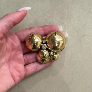 Изящная круглая брошь в руке: несколько золотистых сфер и маленькие сияющие кристаллы на фоне кожи руки с маникюром.