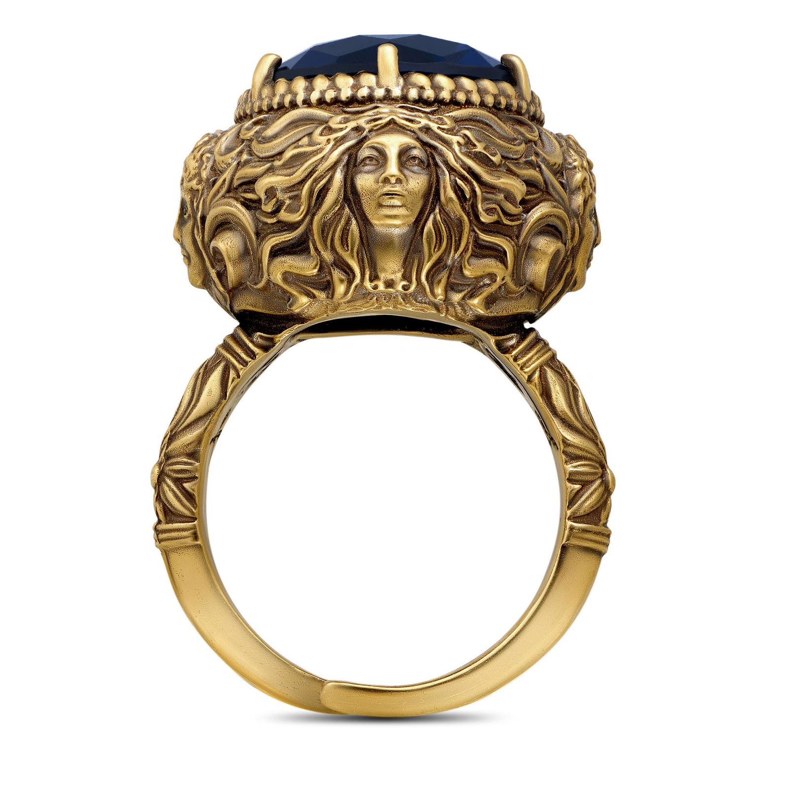Боковой план кольца с позолоченным корпусом и барельефным изображением лица, крупный синий камень сверху и декоративные узоры.