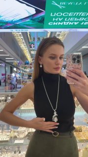 Фотография в зеркале демонстрирует длинную цепочку с медальоном Claudio Canzian, витрина магазина и потолочные панели торгового центра на заднем плане.