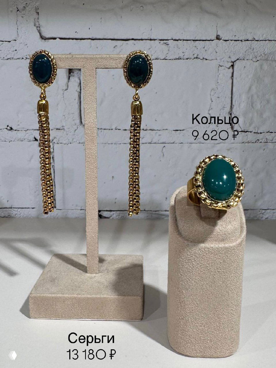 Серьги‑кисти и золотистое кольцо Claudio Canzian с насыщенно зелёным агатом на фоне белой кирпичной стены и ценой на изображении.