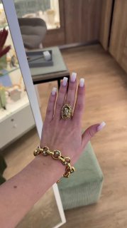 Крупный план руки с массивным золотым браслетом и декоративным кольцом Claudio Canzian; в интерьере бутика видна мягкая мебель и прилавок.