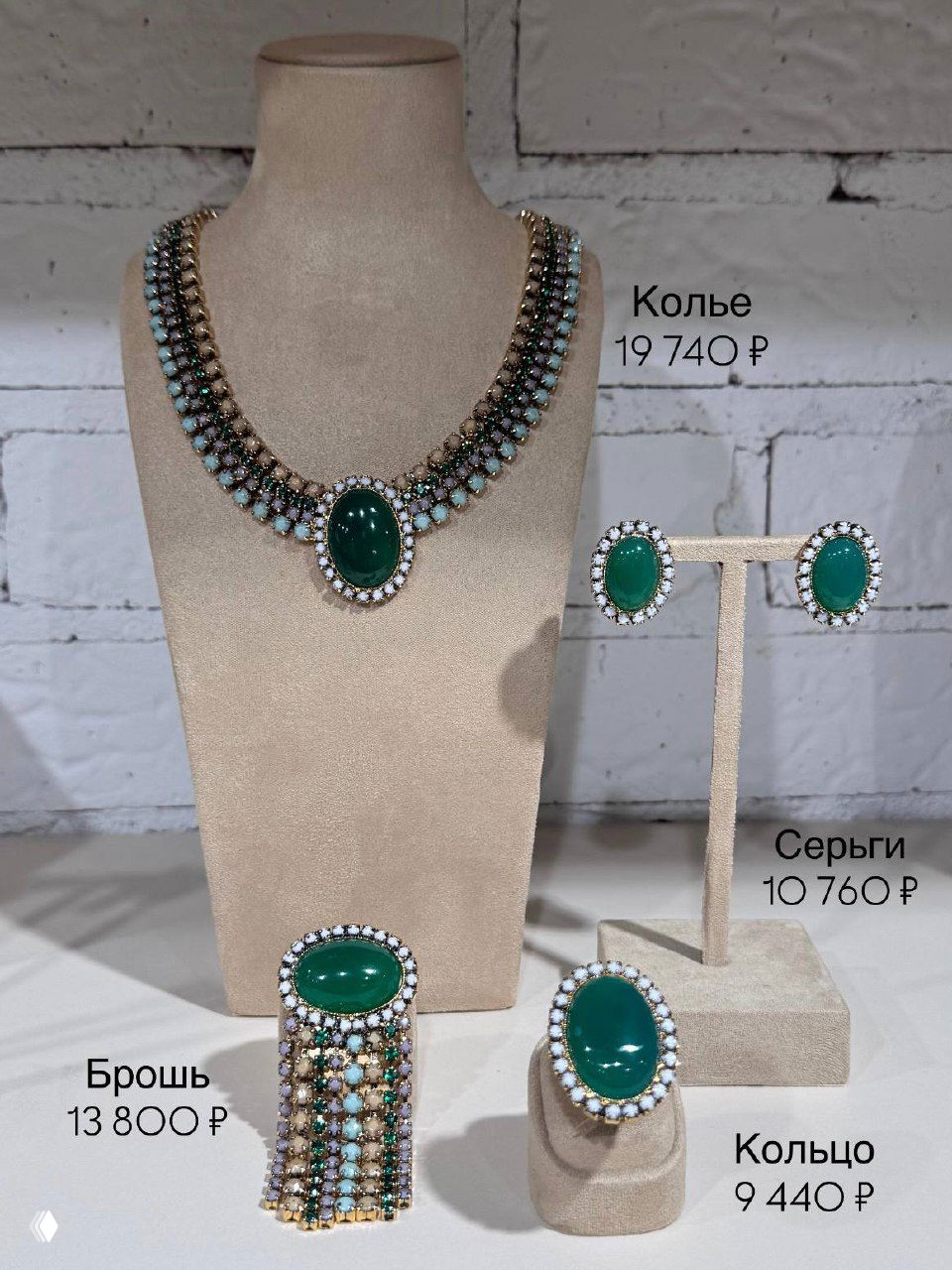 Ожерелье и серьги Claudio Canzian с центральным зелёным кабошоном и брошь внизу, расположение на манекене и ценники видны на фото.