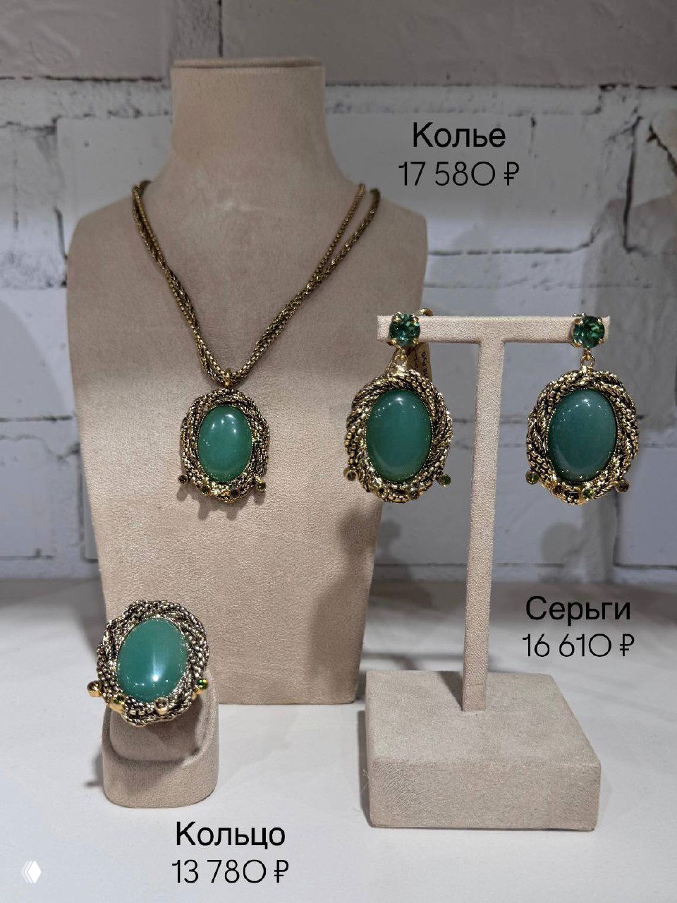 Пара серьг с подвесками из прозрачных кристаллов и кольцо с тёмно‑зелёным агатом на бежевом фоне витрины, цена указана рядом.