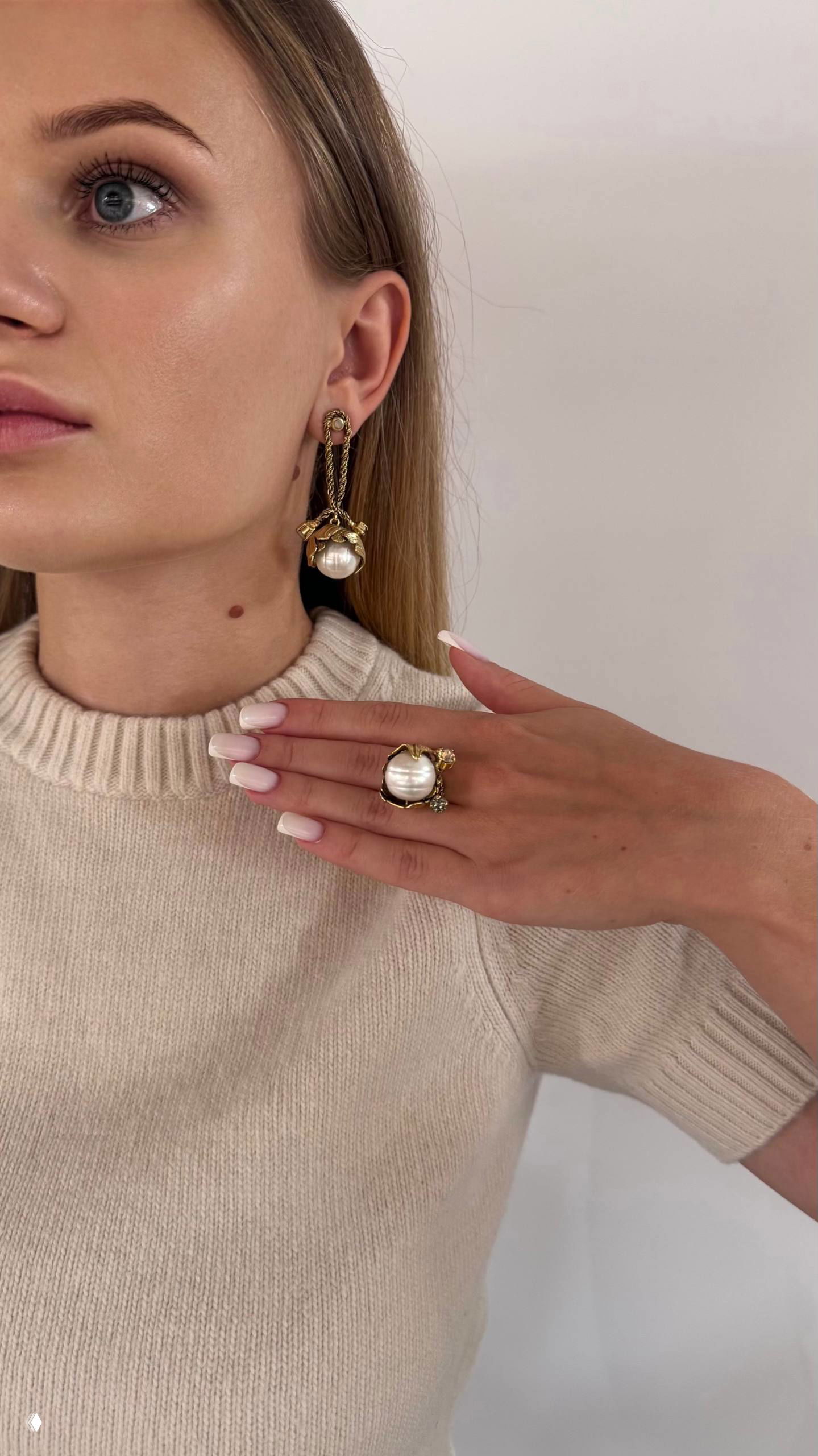 Близкий портрет профиля женщины с подвесной золотой серьгой и крупным жемчужным кольцом — фокус на фактуре металла и естественном блеске жемчуга.