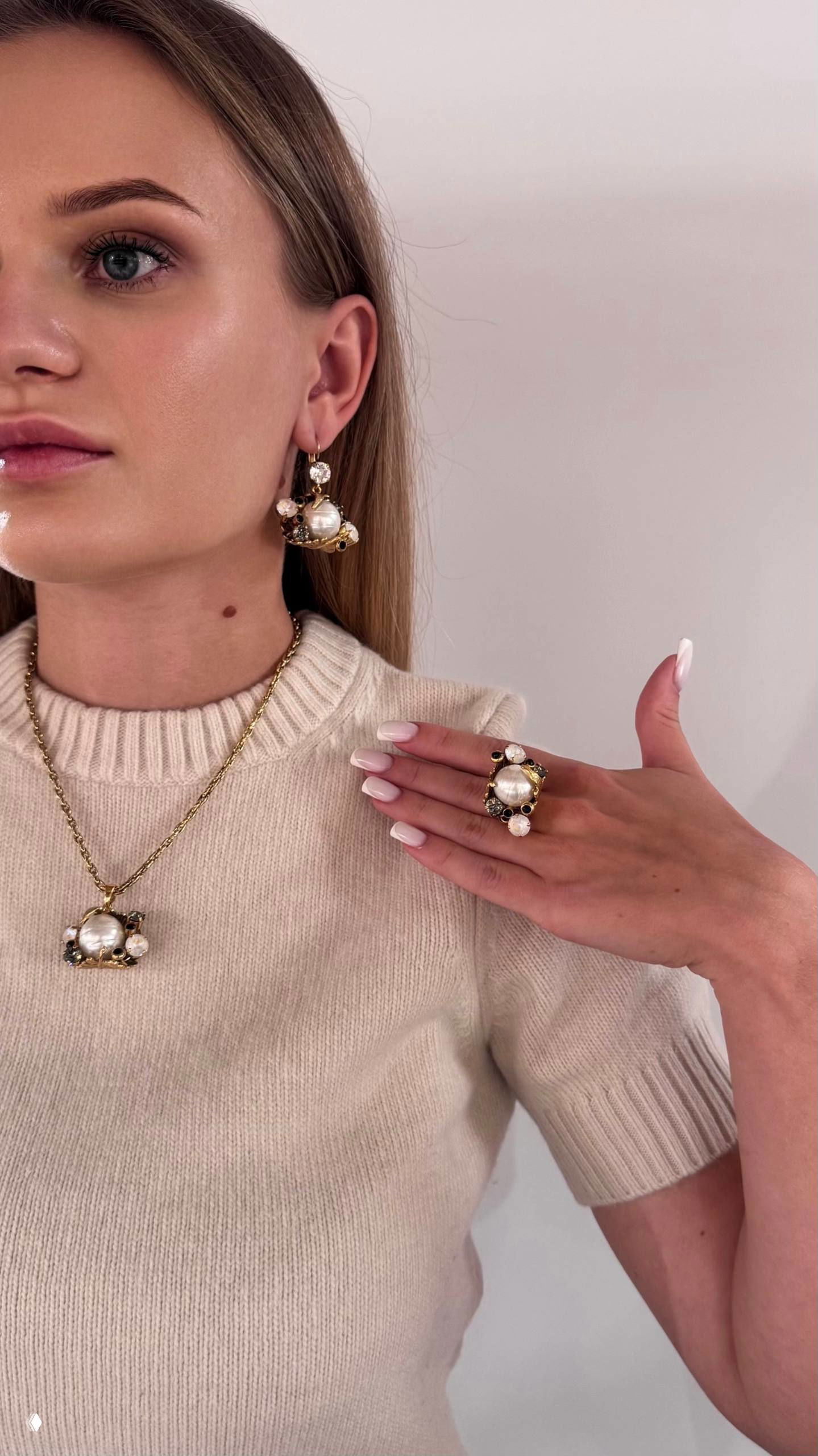 Портрет девушки в светлом свитере и длинным золотым колье с жемчужным подвесом; на пальце крупное жемчужное кольцо — элегантная студийная композиция.