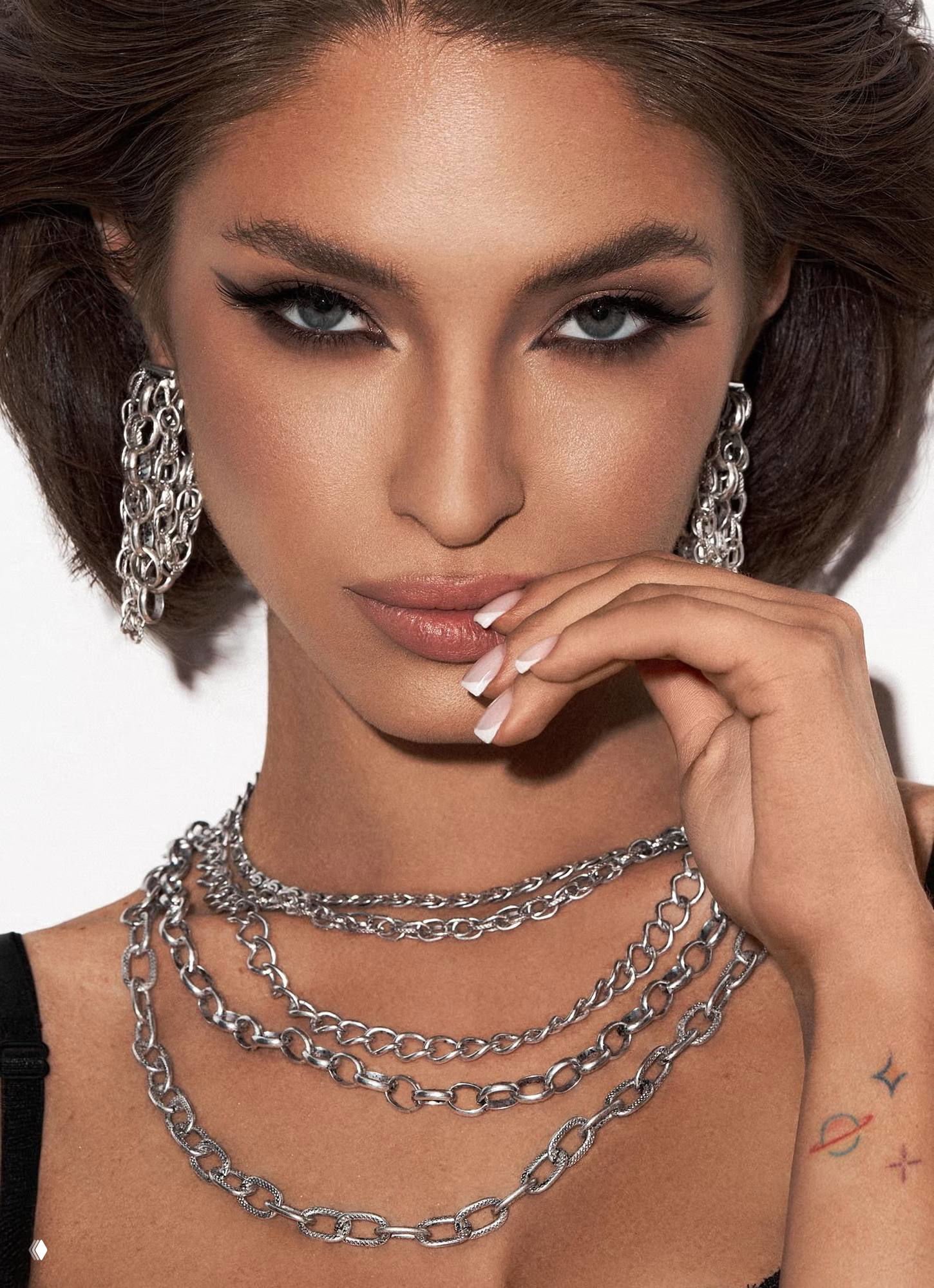 Модель в серебристых украшениях Claudio Canzian: крупный портрет, видны серьги и многослойные цепочки на шее, образ стилизован под рекламу бренда.