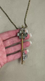 Крупный план необычного ключа: несколько прозрачных вставок и геометрическая подвеска на золотистой ножке, держат на ладони у маникюра.