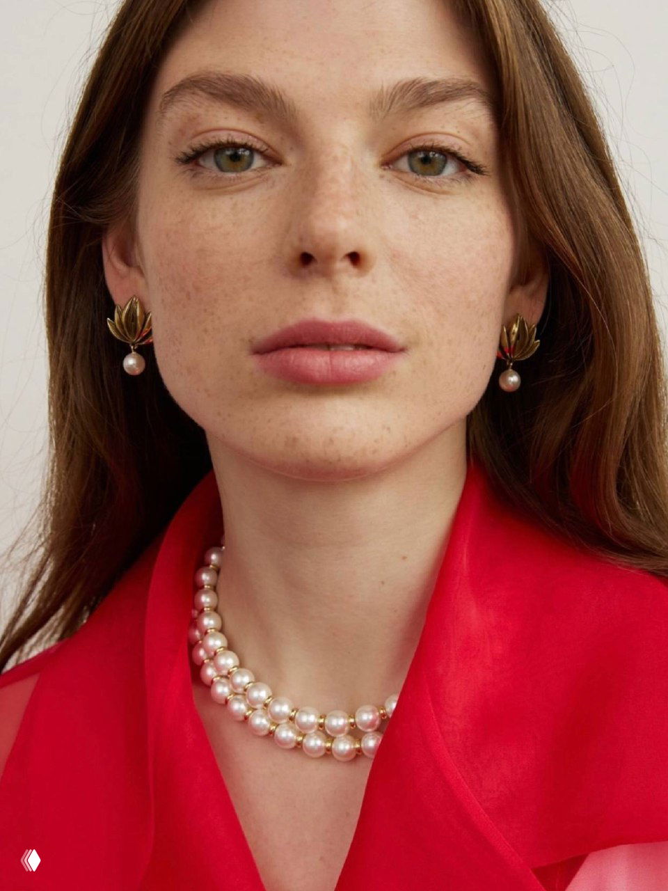 Крупный план лица модели в красном наряде и двойном жемчужном ожерелье Fiore di Firenze, акцент на серьгах-подвесках и естественном макияже.