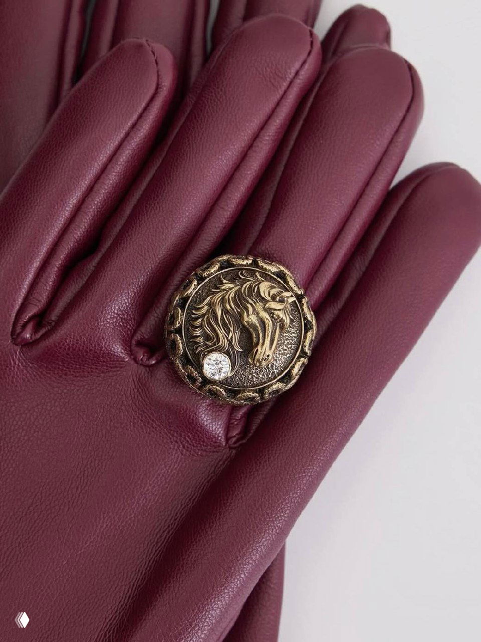 Крупный план бордовых кожаных перчаток с декоративной металлической пуговицей-брошей в форме головы лошади и кристаллом — аксессуар в стиле Fiore di Firenze.