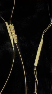 Крупный план тонких золотых деталей и застёжек на чёрном фоне; видна текстура металла, элементы дизайна и способы соединения звеньев.