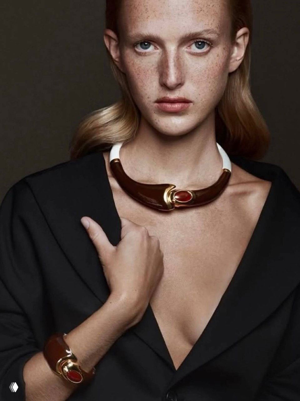 Студийный портрет модели в крупном колье: элегантное колье с тёмными и золотистыми вставками на шее, акцент на форме, минималистичный фон и профессиональная съёмка.