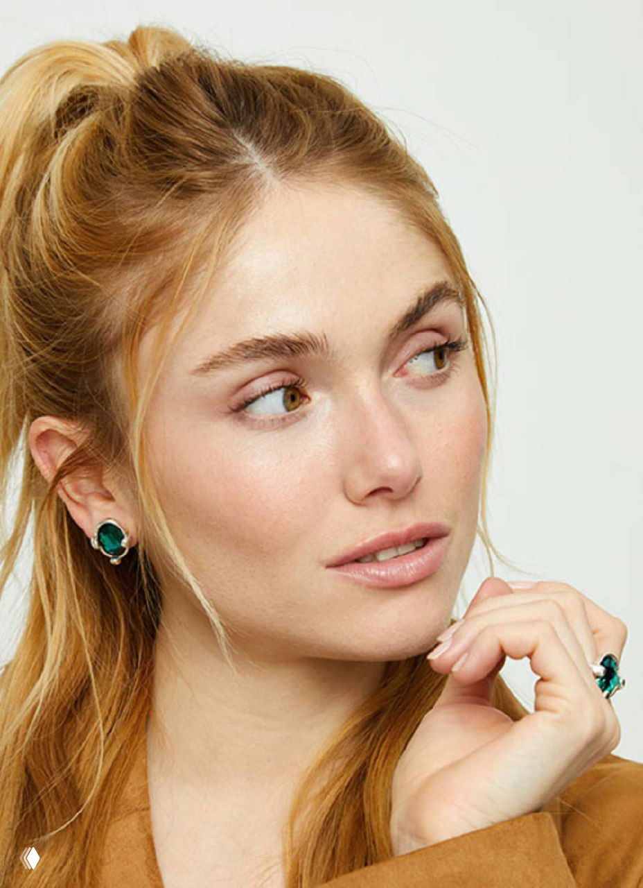 Портрет модели в украшениях UNOde50: крупный план серьг и кольца, мягкий свет, акцент на лице и стильных аксессуарах бренда.