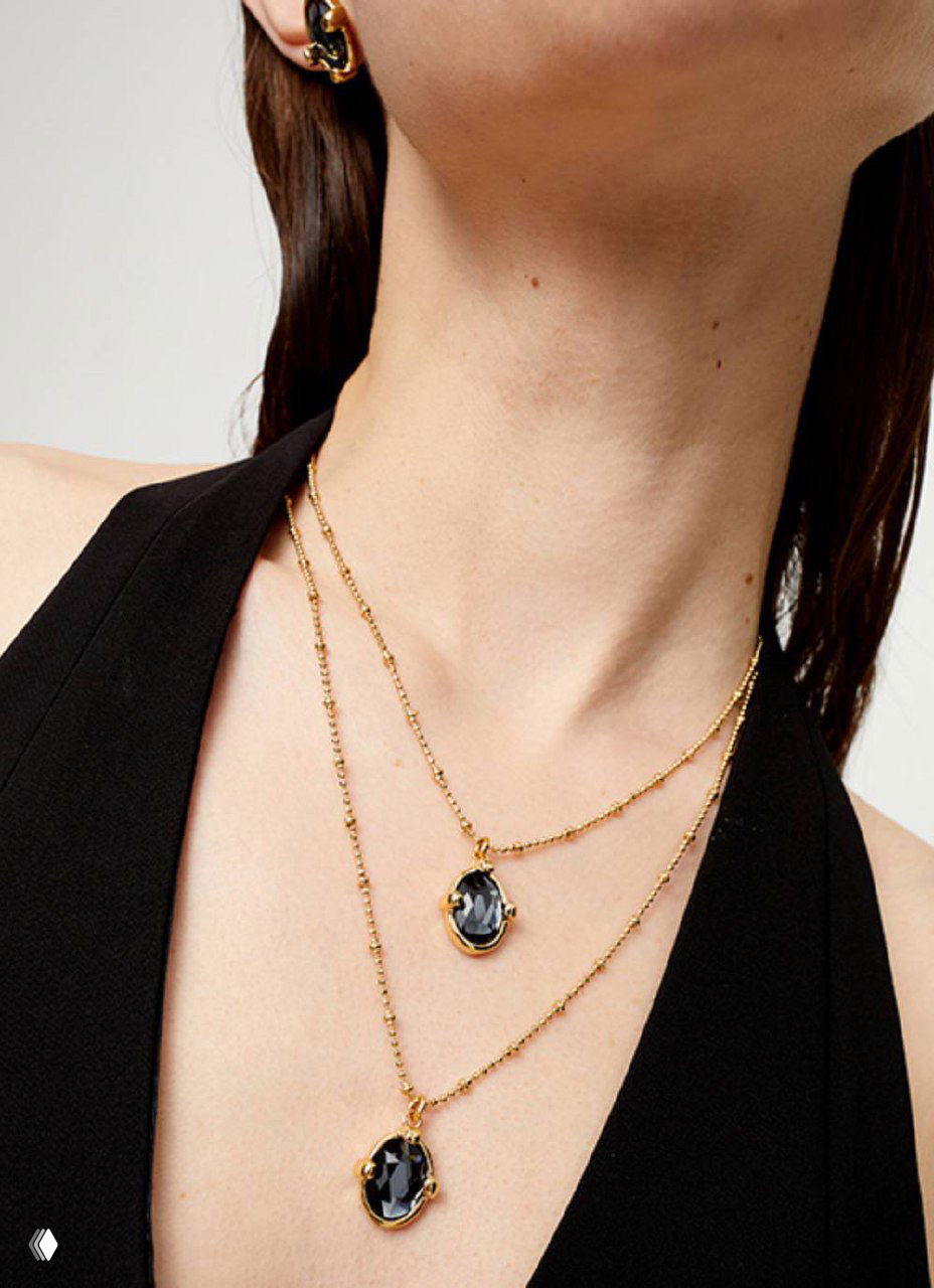 Крупный план двойной подвески на длинной цепочке UNOde50 на шее модели — две изящные подвески разного размера, блеск металла.