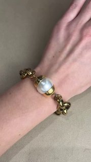 Крупный план браслета с большой белой жемчужиной в золотой оправе и массивной цепью на запястье модели — изделие из коллекции Claudio Canzian.