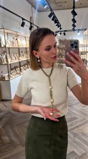 Модель держит подвеску в ладони, видно длинное ожерелье и серьги на фоне торгового зала Rosone — демонстрация дизайна и посадки украшений.