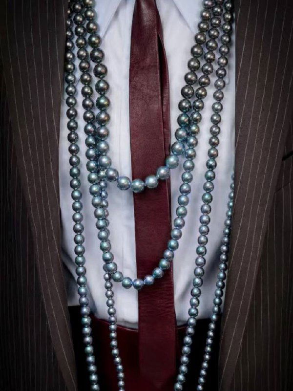 Несколько нитей жемчужных ожерелий цвета «перо павлина» на фоне одежды — показано сочетание украшения с деловым стилем.