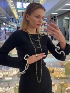 Женская витрина магазина: модель у зеркала примеряет длинные цепи и украшения коллекции Fiore di Firenze на фоне стеклянных витрин с бижутерией.