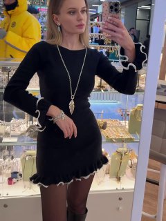 Модель позирует у витрины с несколькими украшениями Ciclon: звёздный кулон на длинной цепочке и минималистичные серьги на фоне торговой стойки.