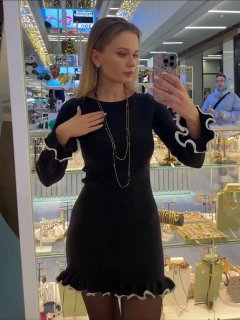 Модель у витрины примеряет колье и демонстрирует образ с несколькими слоями украшений, отражение в зеркале и элементы торгового зала видны вокруг.